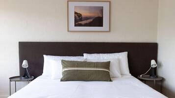 A neatly made bed with white linens and two pillows, a framed picture on the wall, and two bedside lamps on either side.