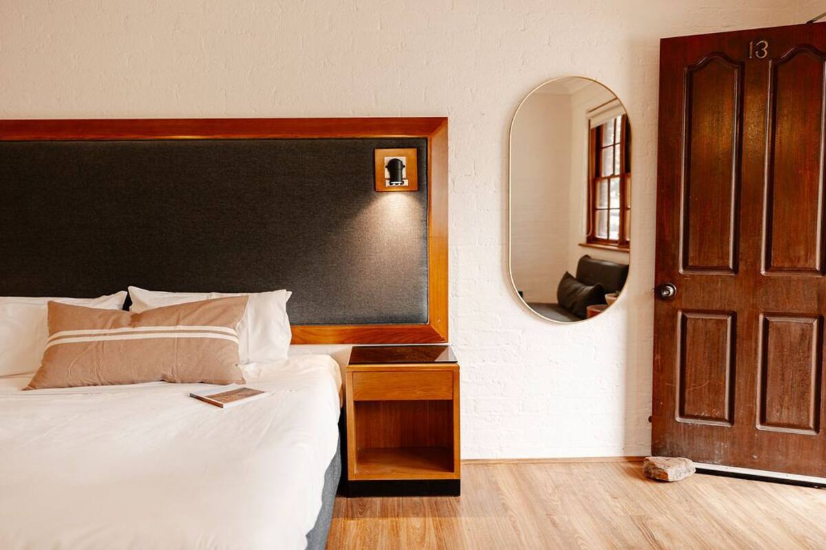 A neatly made bed with a wooden headboard, a bedside table, and a mirror on the wall.