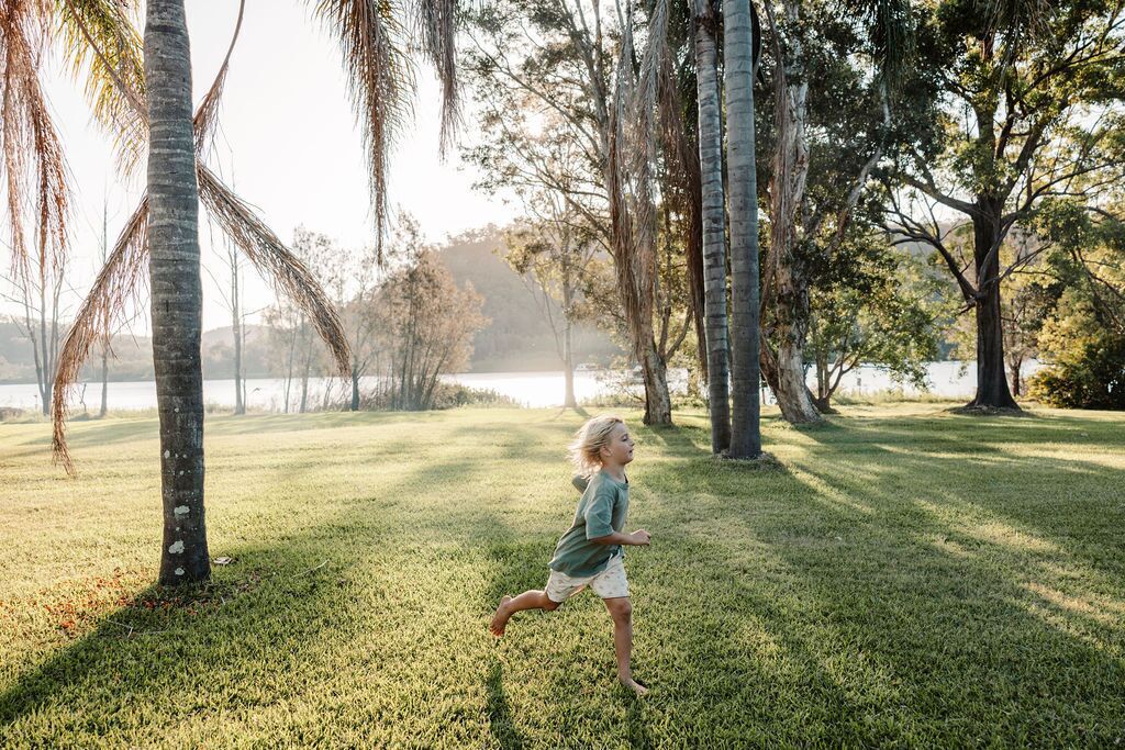 A child running in a grassy park with trees and a body of water in the background.