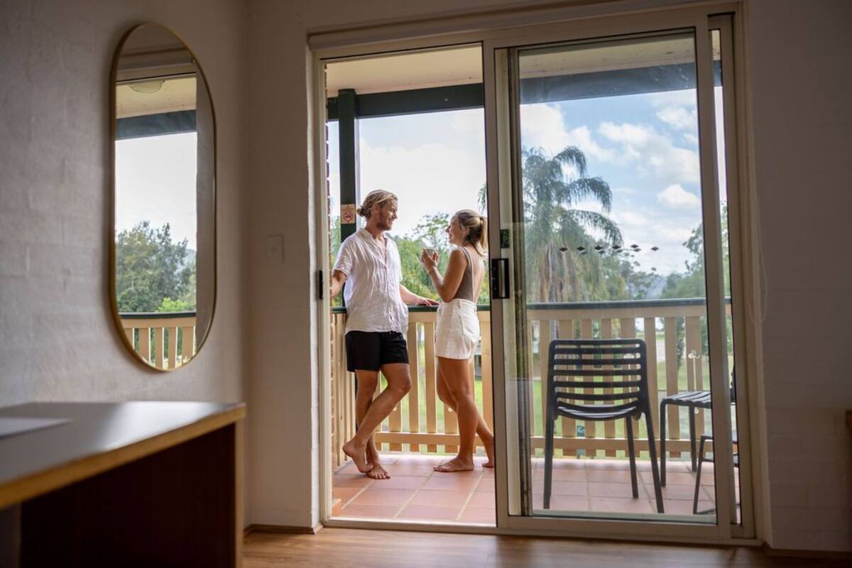 A room with a sliding glass door leading to an outdoor balcony with a wooden railing and a chair.