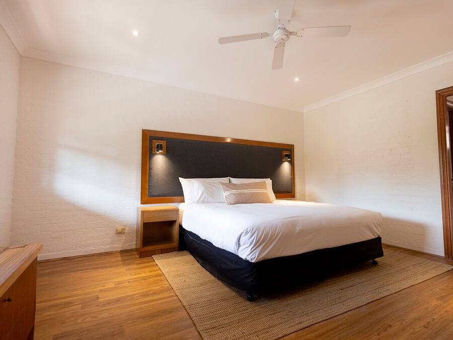 Une chambre à coucher avec un lit, des tables de chevet en bois, un ventilateur de plafond et un grand miroir.