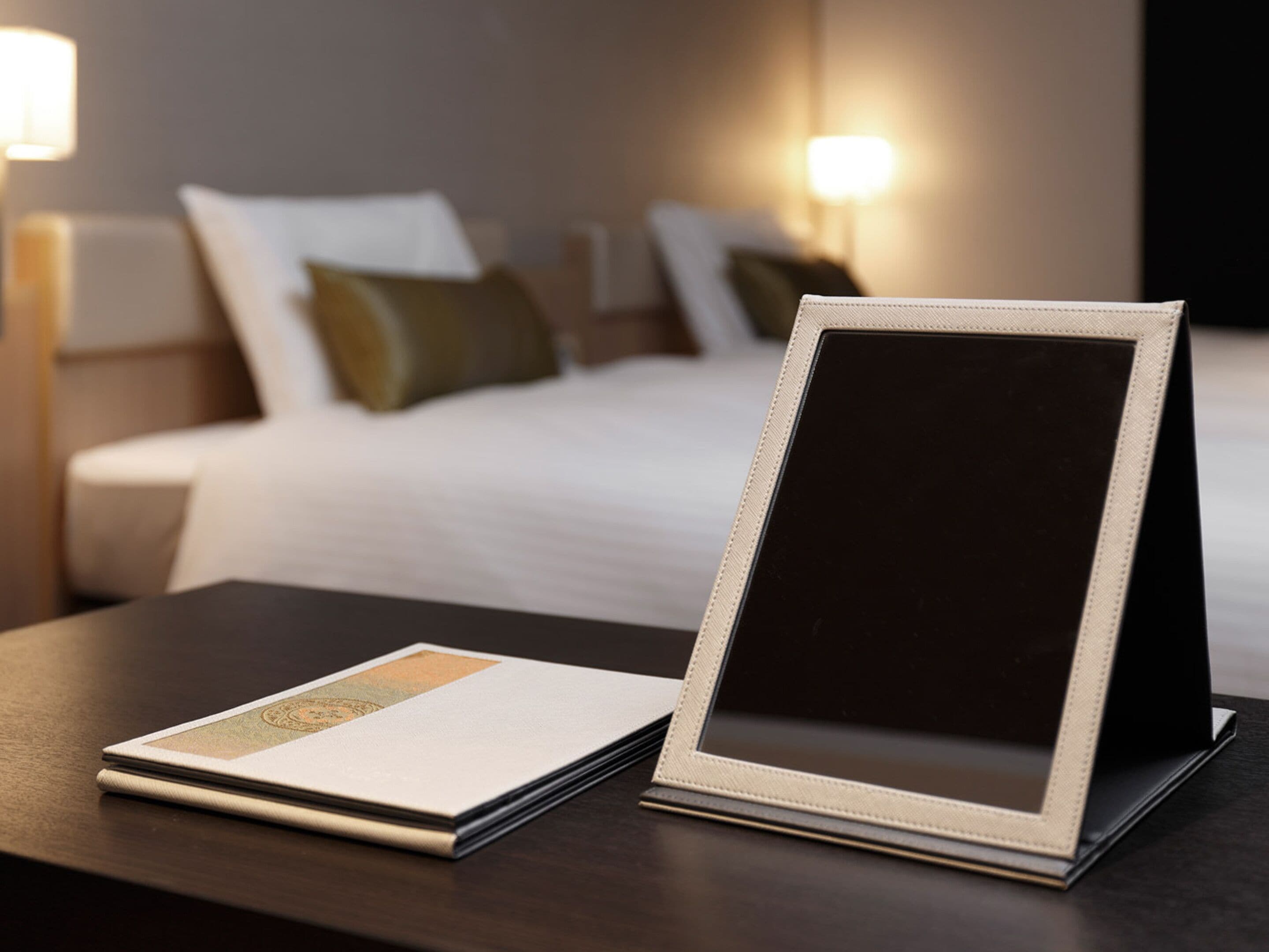 A neatly arranged hotel room with a bed, bedside lamps, and a table with a framed picture and a brochure.
