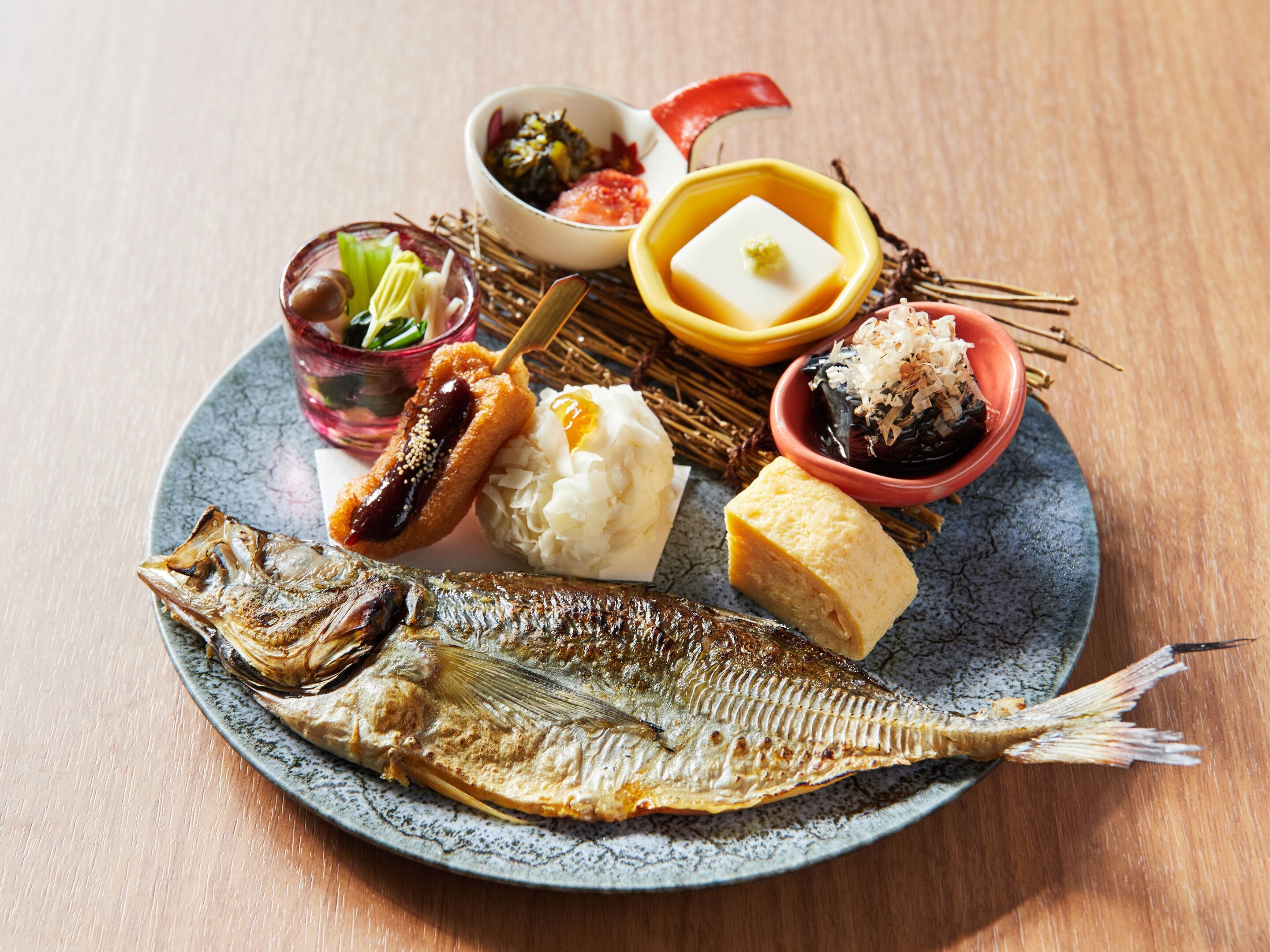 Een bord met een hele vis, diverse bijgerechten en een klein schaaltje saus.