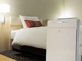 A hotel room with a bed, a bedside lamp, and a white air conditioning unit.