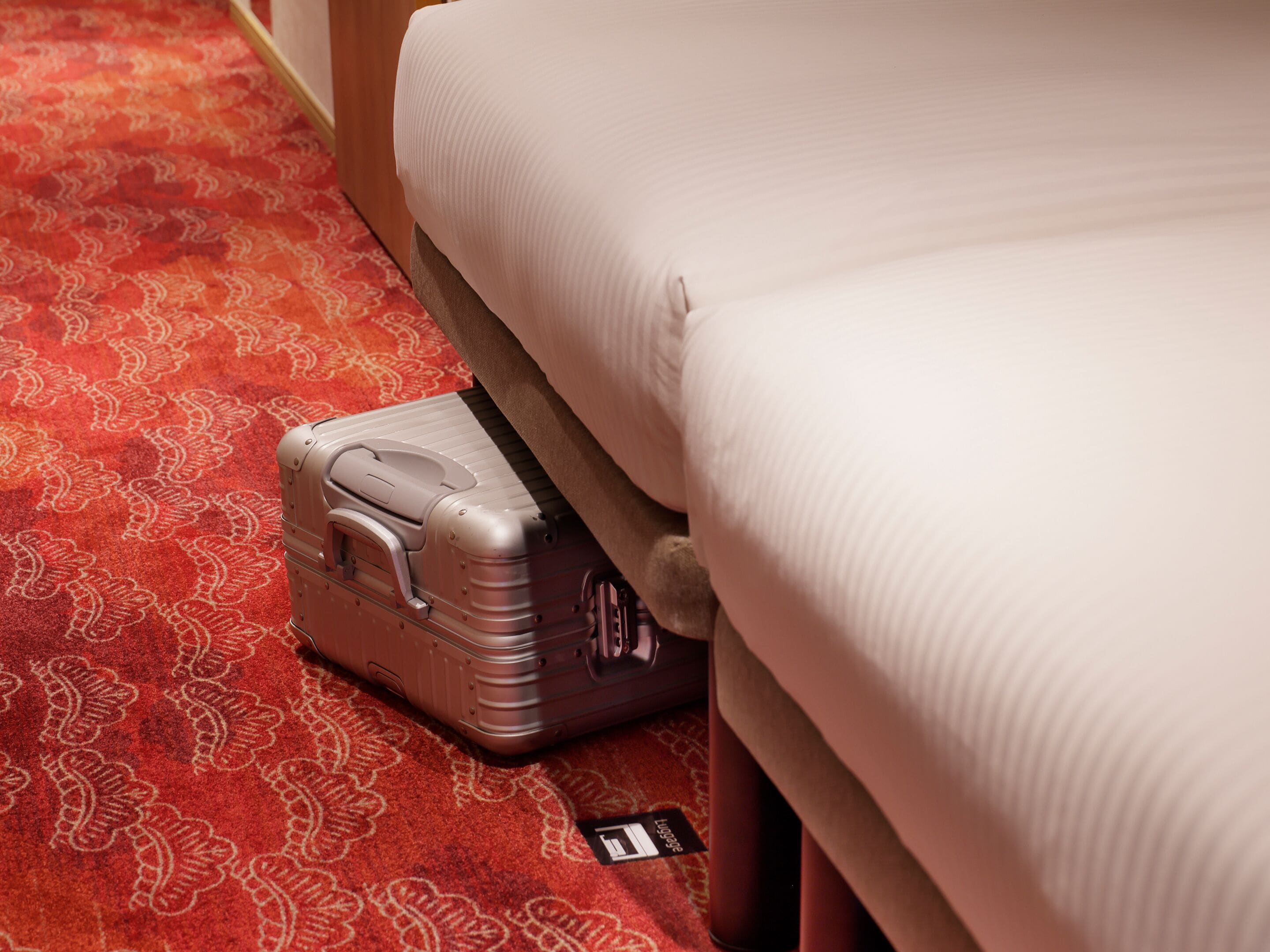 A bed with a suitcase on a patterned carpet.