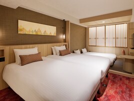 A hotel room with two beds, a large painting, a window with vertical blinds, and a small table.