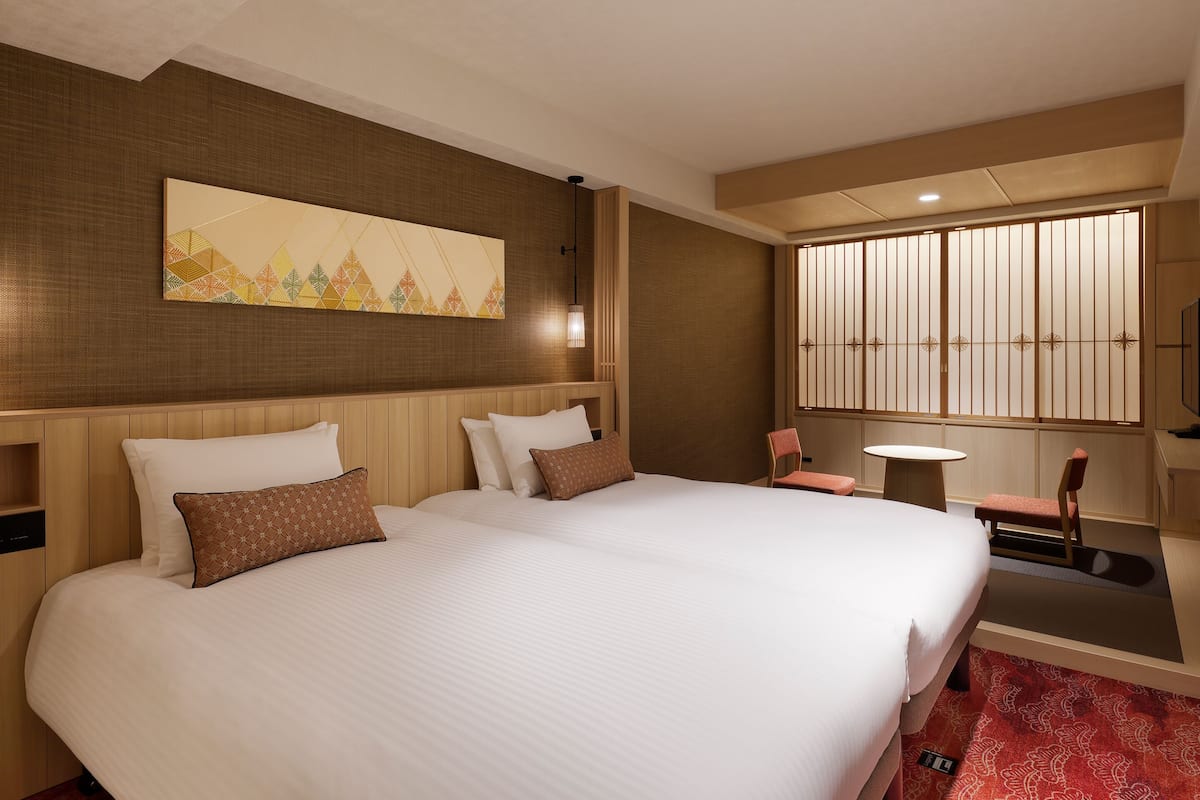 Ein Hotelzimmer mit einem großen Bett, einem kleinen Tisch, einem Sessel, einem Fernseher und einer Wanddekoration.