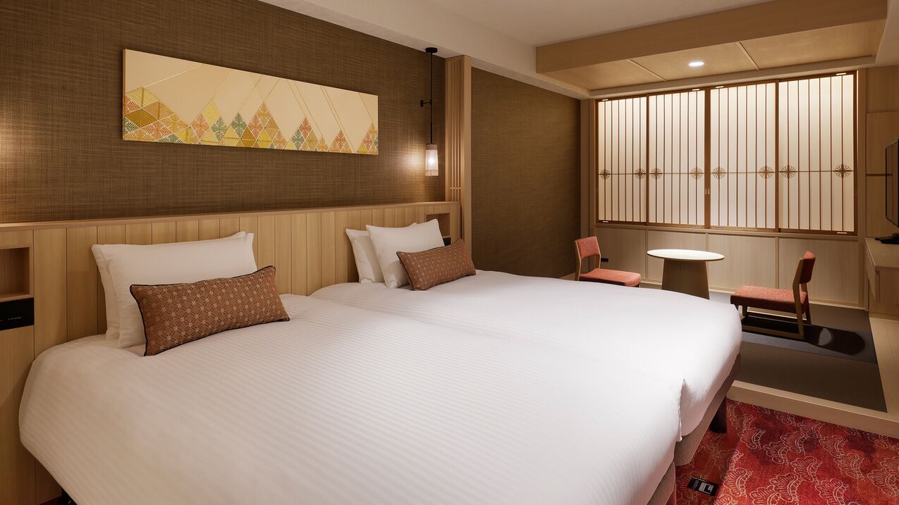 Habitación de hotel con una cama grande, una mesita, una silla, un televisor y un separador decorativo.