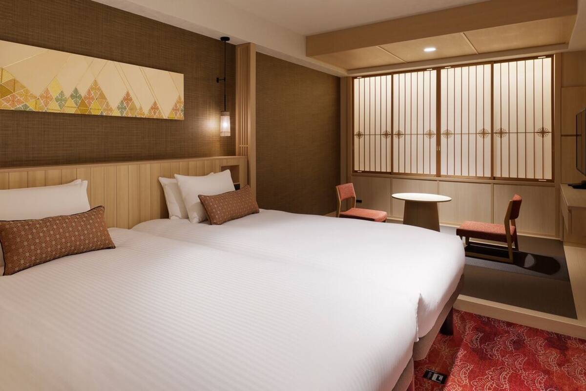 Ein Hotelzimmer mit einem großen Bett, einem kleinen Tisch, einem Sessel, einem Fernseher und einem dekorativen Raumteiler.