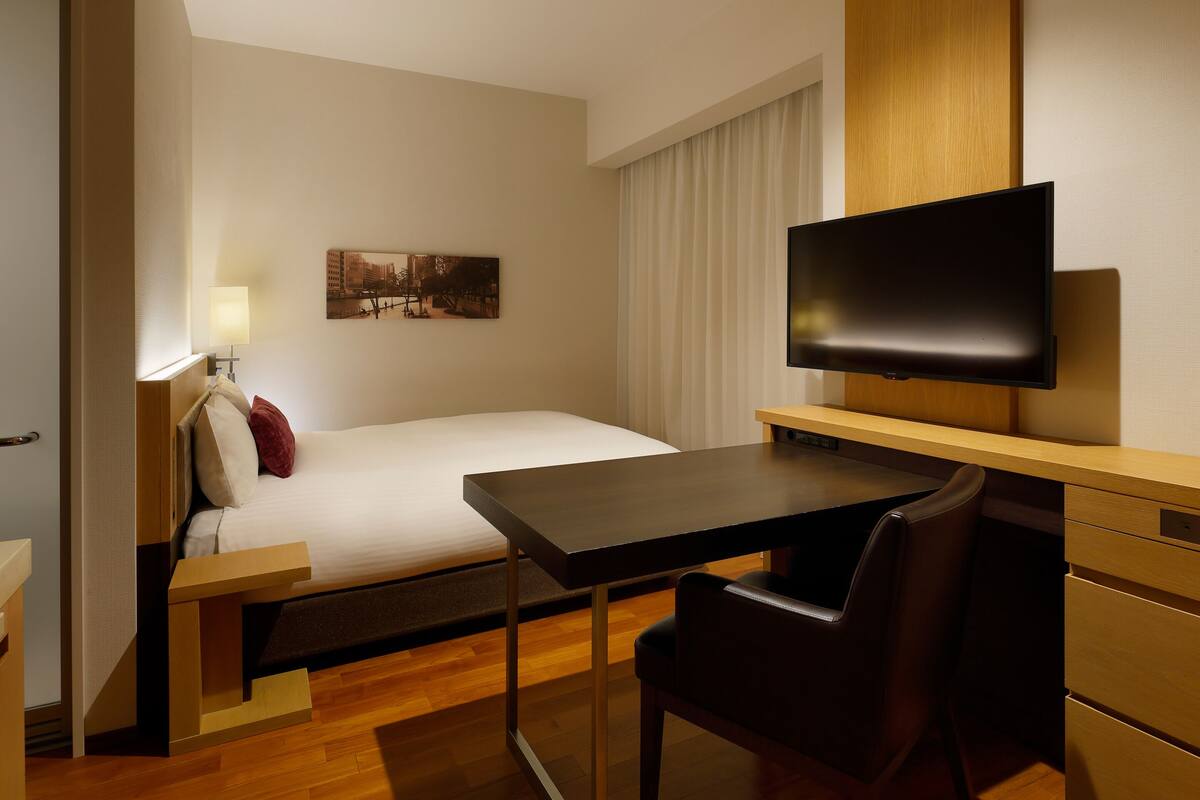 Une chambre d’hôtel équipée d’un lit, d’un bureau, d’une chaise, d’une télévision et d’une fenêtre avec des rideaux.