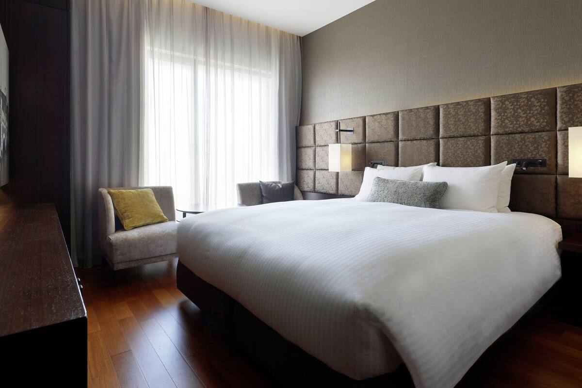 Une chambre d’hôtel avec un grand lit, un canapé, un bureau et une fenêtre avec des rideaux.