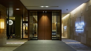 Een moderne hotelentree met een houten trap, een glazen deur en een bord met Japanse karakters.