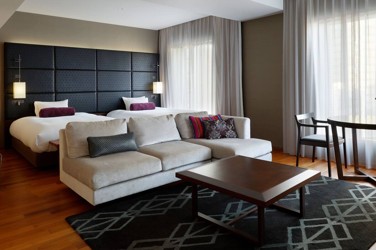 Une chambre d’hôtel comprenant un lit, un canapé, une table basse, une table à manger et une tête de lit dotée d’un luminaire.