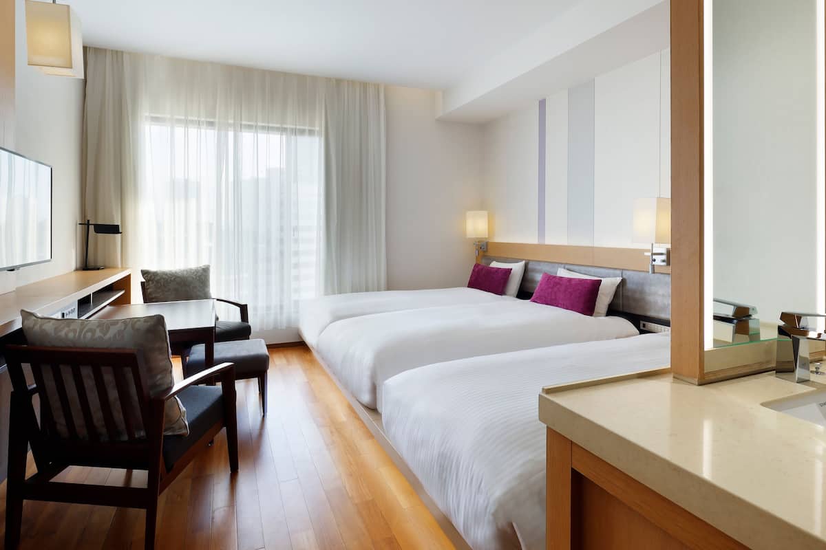 Une chambre d’hôtel avec un lit, un bureau et une chaise, une télévision et une fenêtre avec des rideaux.