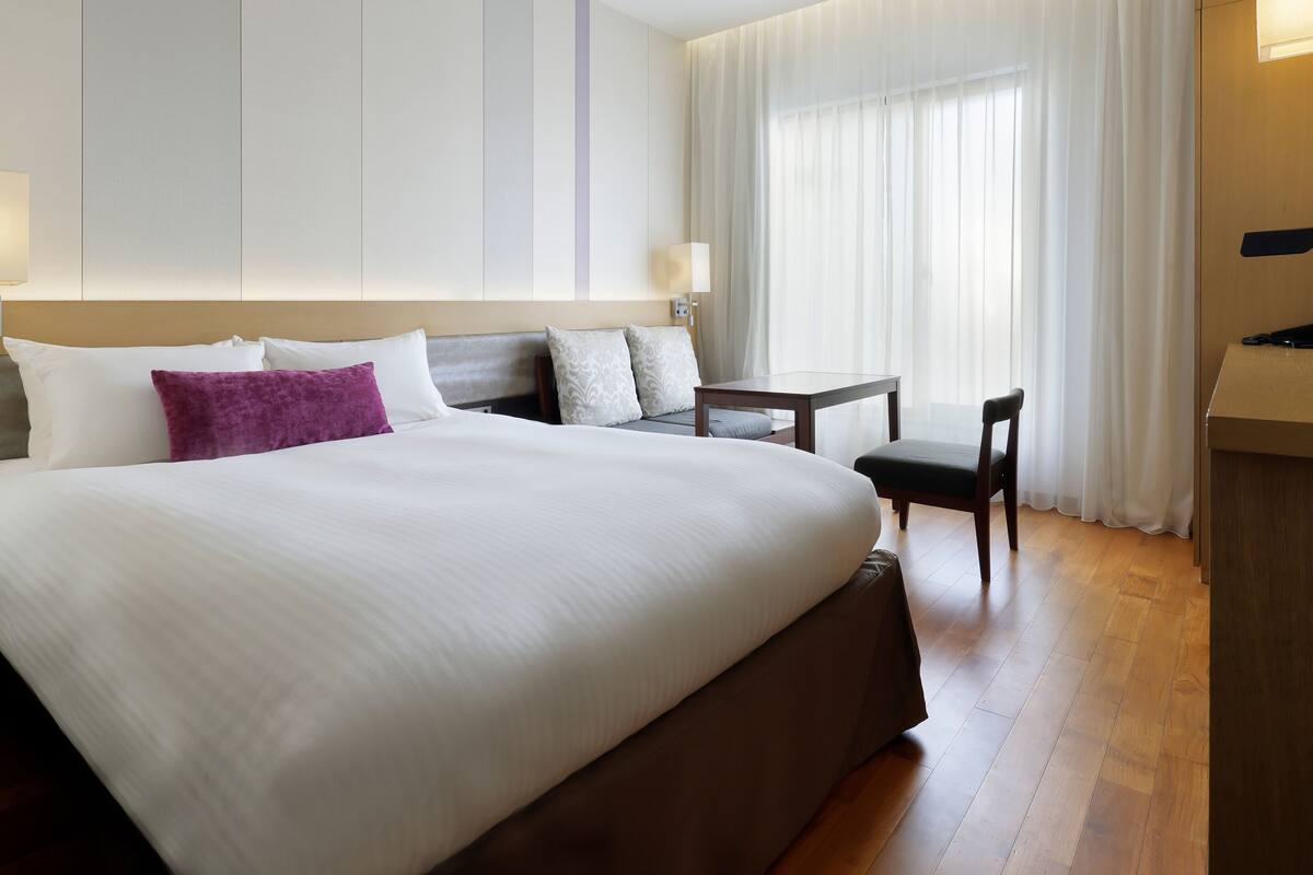 Une chambre d’hôtel avec un grand lit, un bureau, une chaise et une fenêtre avec des rideaux.