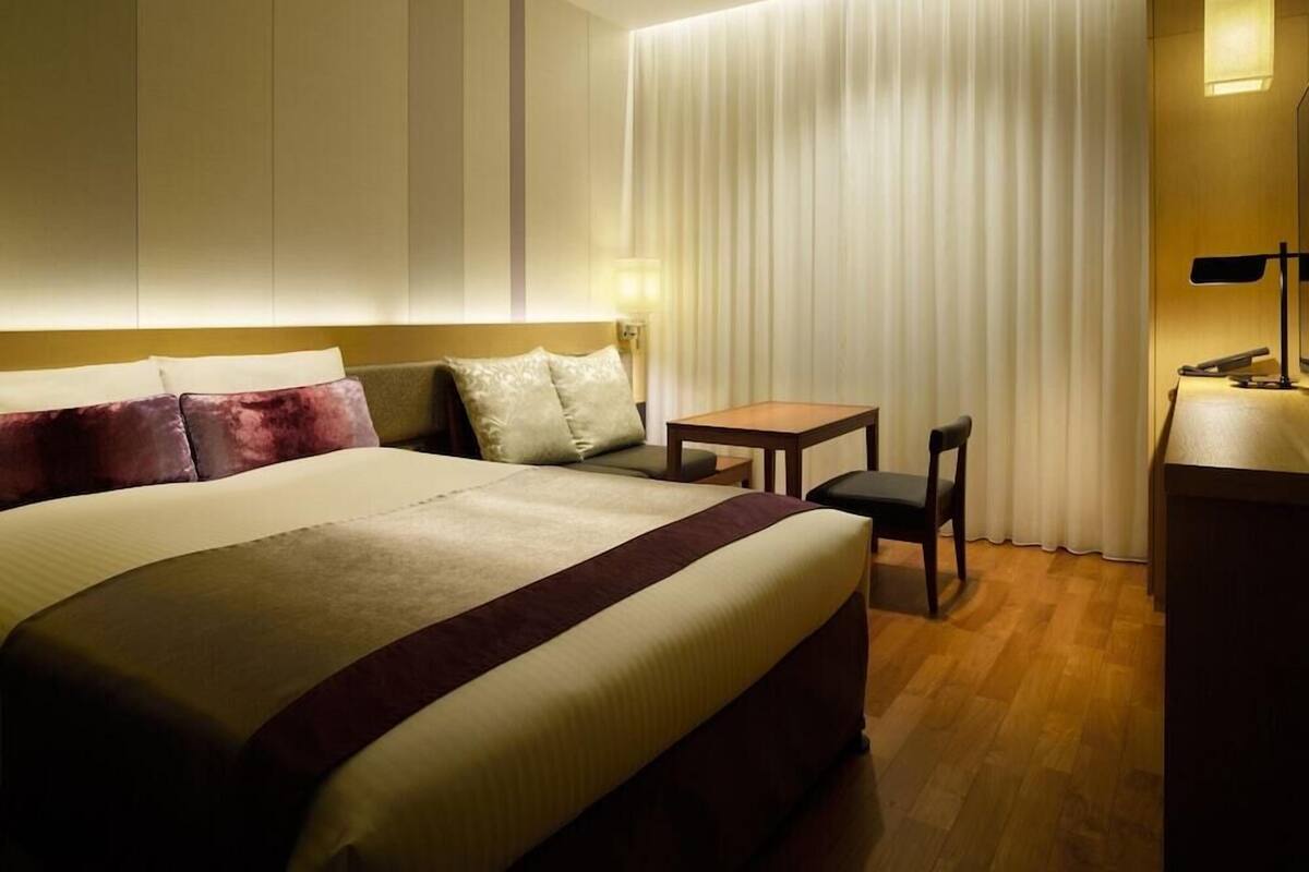 Une chambre d’hôtel avec un lit, un bureau, une chaise et une lampe.