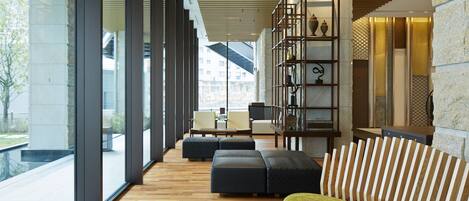 A modern interior with a wooden floor, large windows, a striped sofa, and a bookshelf with decorative items.