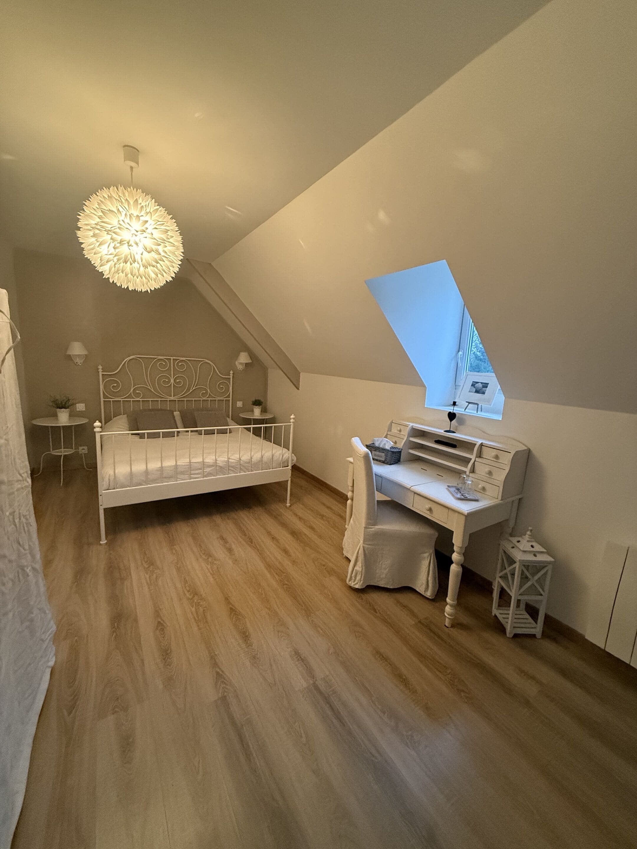 A bedroom with a sloped ceiling, a bed, a desk, and a hanging light fixture.