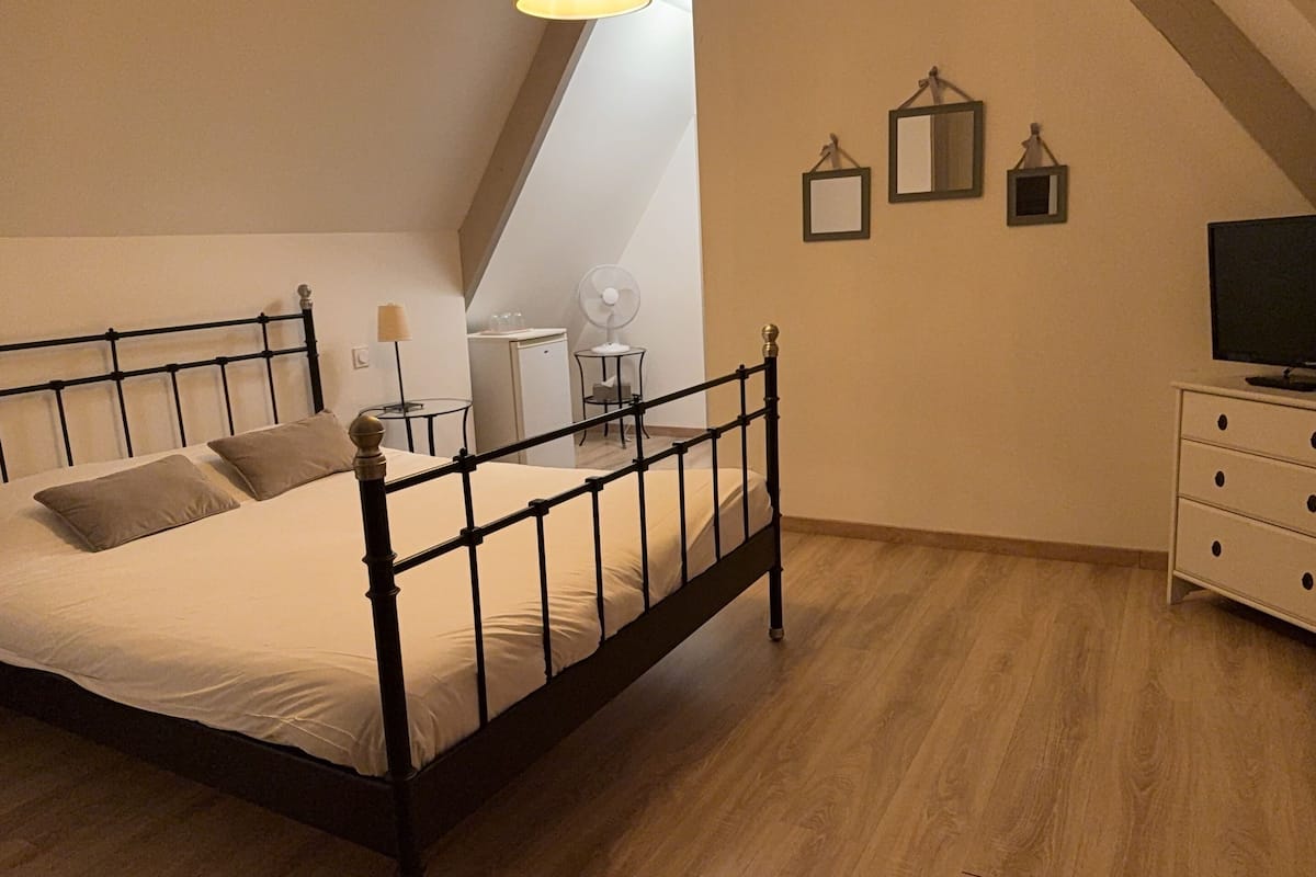 A bedroom with a bed, a desk, a chair, a lamp, a fan, and a TV.