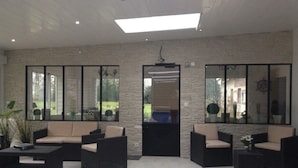 A modern indoor lounge area with stone walls, large windows, and black wicker furniture.