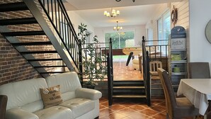A living room with a staircase, a sofa, a dining table, and a chandelier.