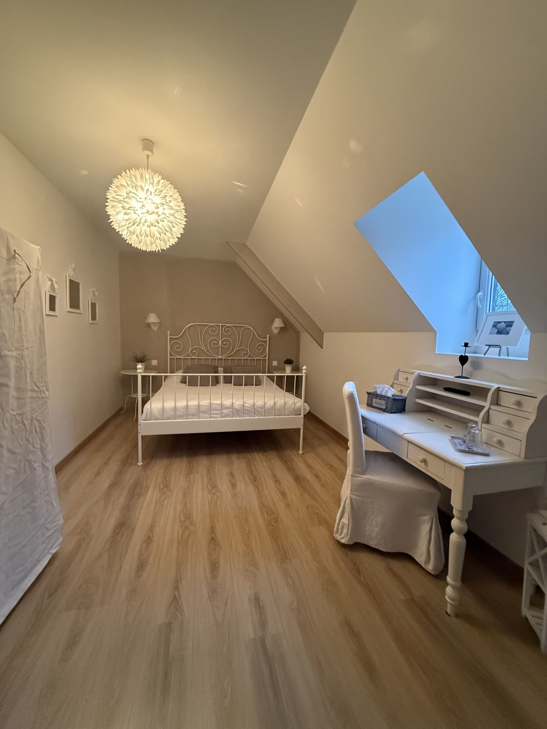 Une chambre avec un plafond en pente, un lit, un bureau et une lucarne.
