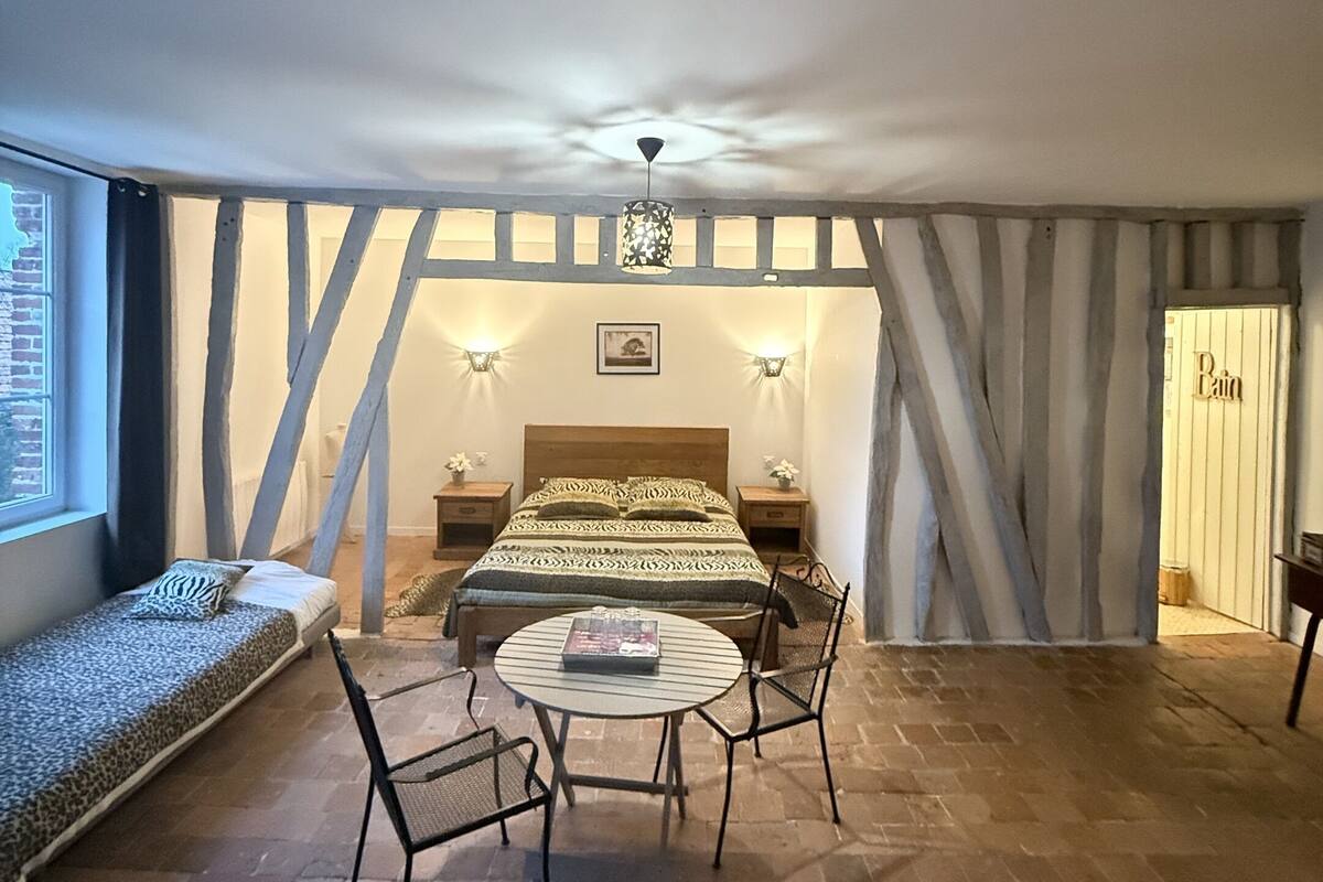 A cozy room with a bed, a round table, and chairs, a window, and a door.