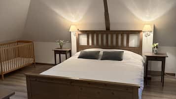 A bedroom with a wooden bed, two bedside tables, a nightstand, a crib, and a sloped ceiling with exposed beams.