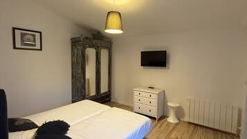 Een slaapkamer met een bed, een dressoir, een spiegel, een televisie en een radiator.