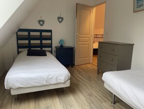 A bedroom with two beds, a nightstand, a dresser, and a door leading to another room. - Château de Grèges (Greges)