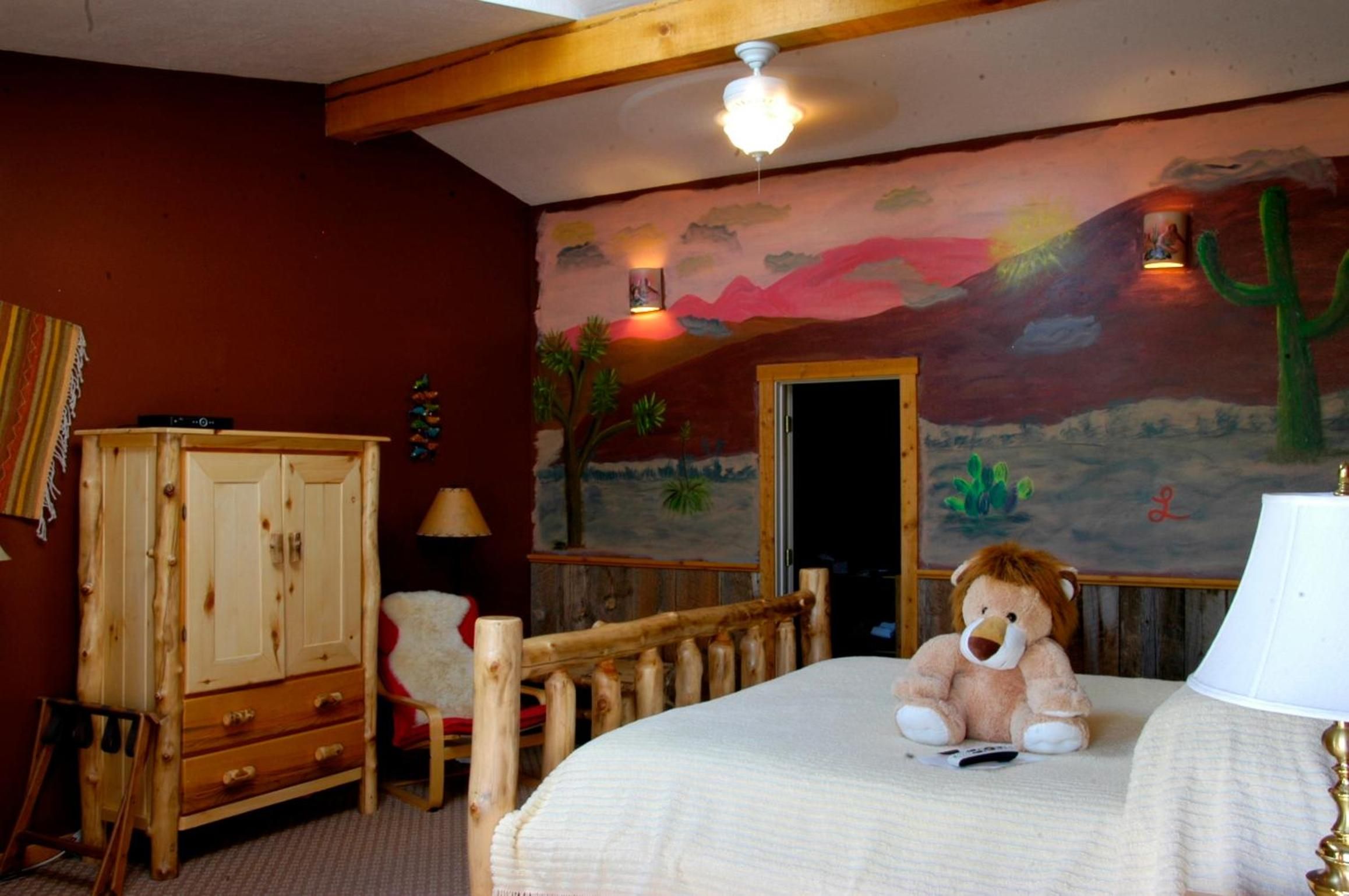A room with a bed, a wooden wardrobe, a chair, a lamp, and a mural on the wall.
