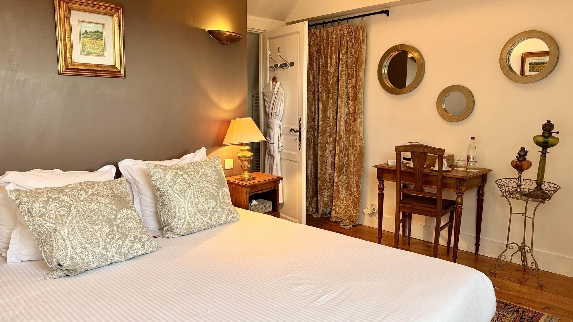 A hotel room with a bed, a table with chairs, a lamp, and a mirror on the wall.