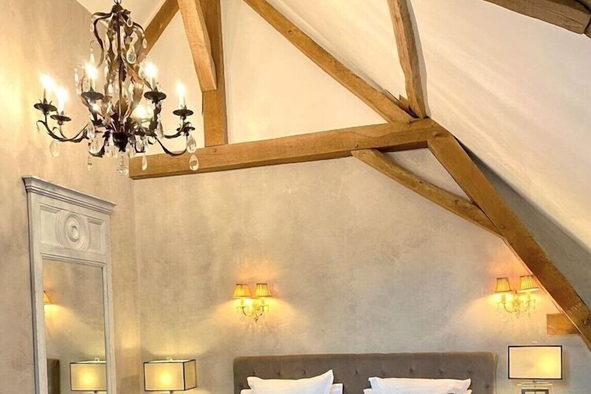 Une chambre à coucher avec un plafond voûté, un lustre, des lampes de chevet, un grand miroir et un tapis à motifs.