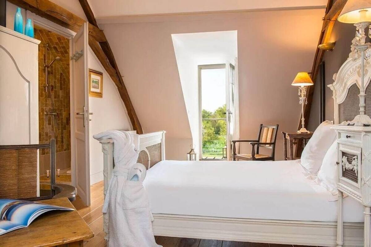 Ein Schlafzimmer mit Bett, Stuhl, Nachttisch, Lampe und Fenster.