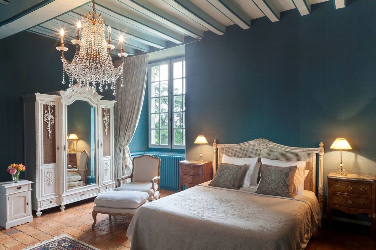 Ein Schlafzimmer mit einem großen Bett, einer Chandelier, einem Kleiderschrank und einem Fenster mit Vorhängen.