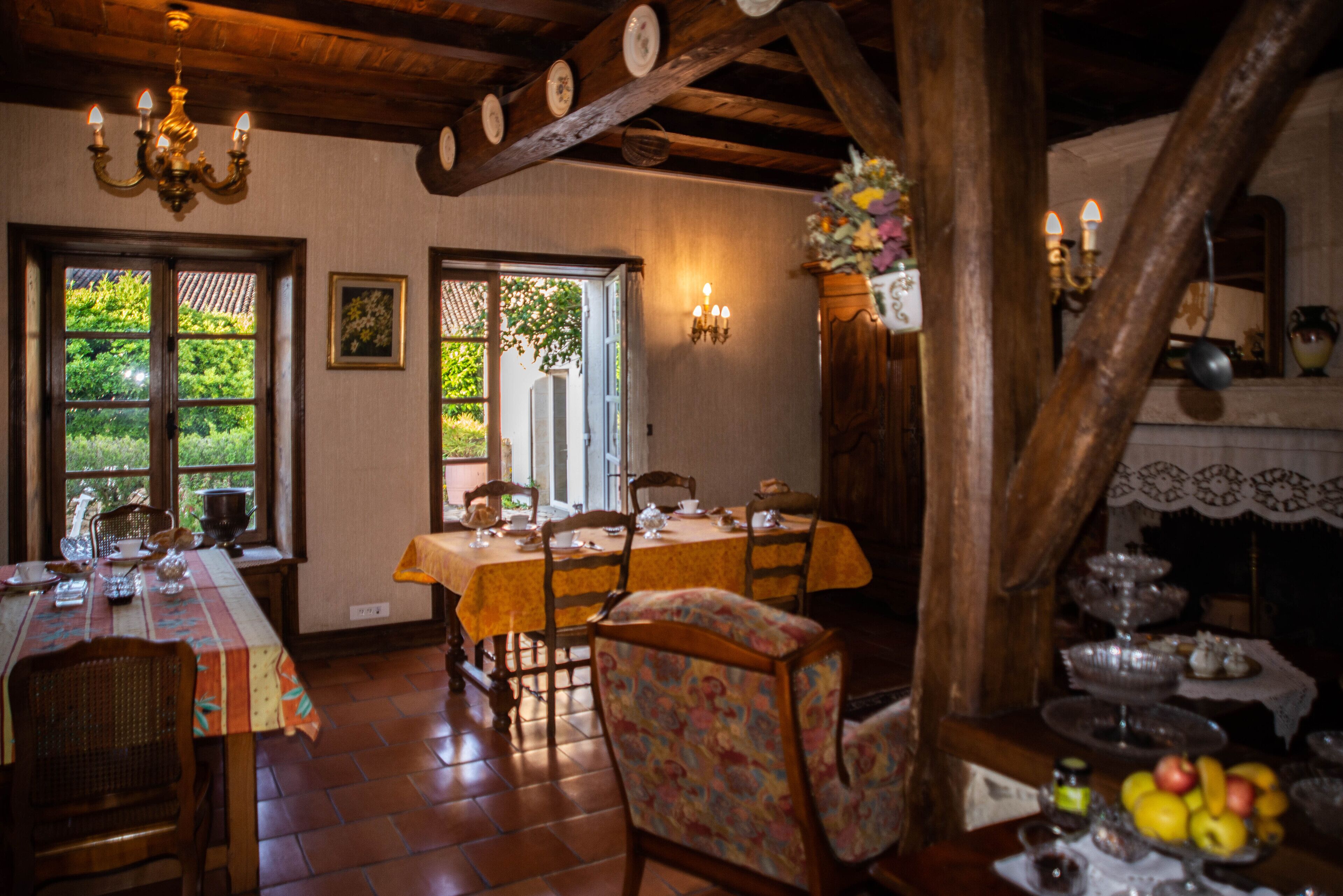 Comedor con mesas y sillas de madera, un candelabro y vistas al exterior con vegetación.