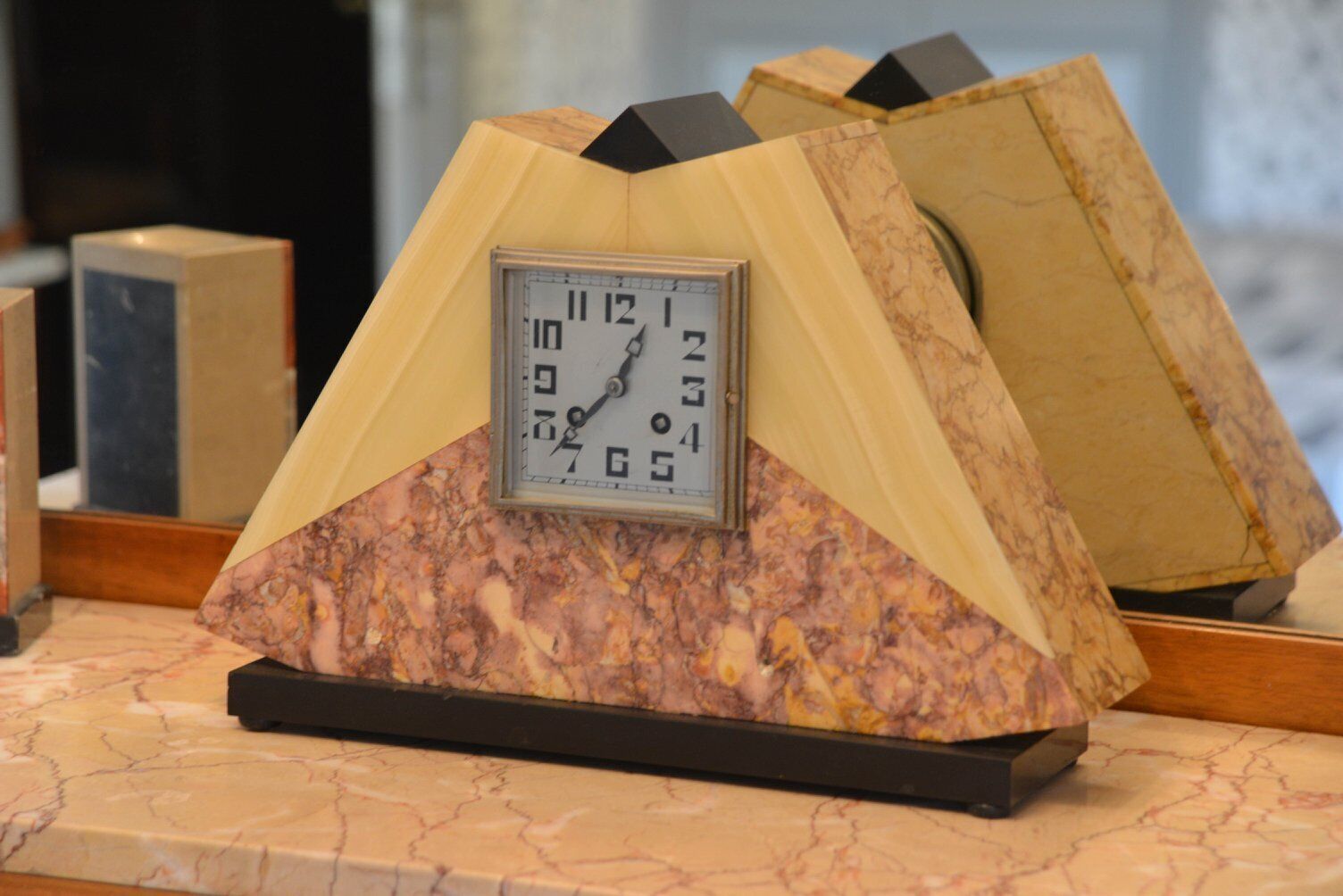 Une horloge dotée d’un socle en marbre et d’un sommet triangulaire, posée sur un comptoir en marbre.