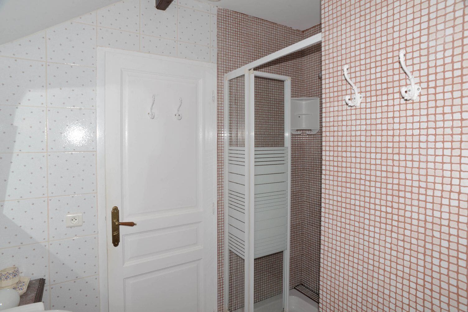 A bathroom with a white door, tiled walls, and a shower area.