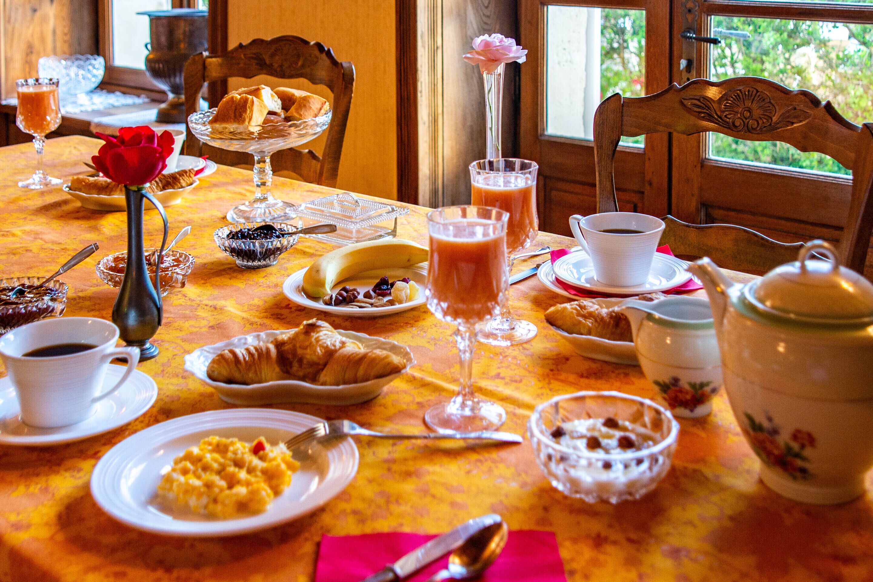 A breakfast table with various food items, including croissants, a banana, and a glass of juice.