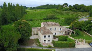 Traditional stone building with a central entrance, surrounded by well-maintained gardens and a vineyard view.