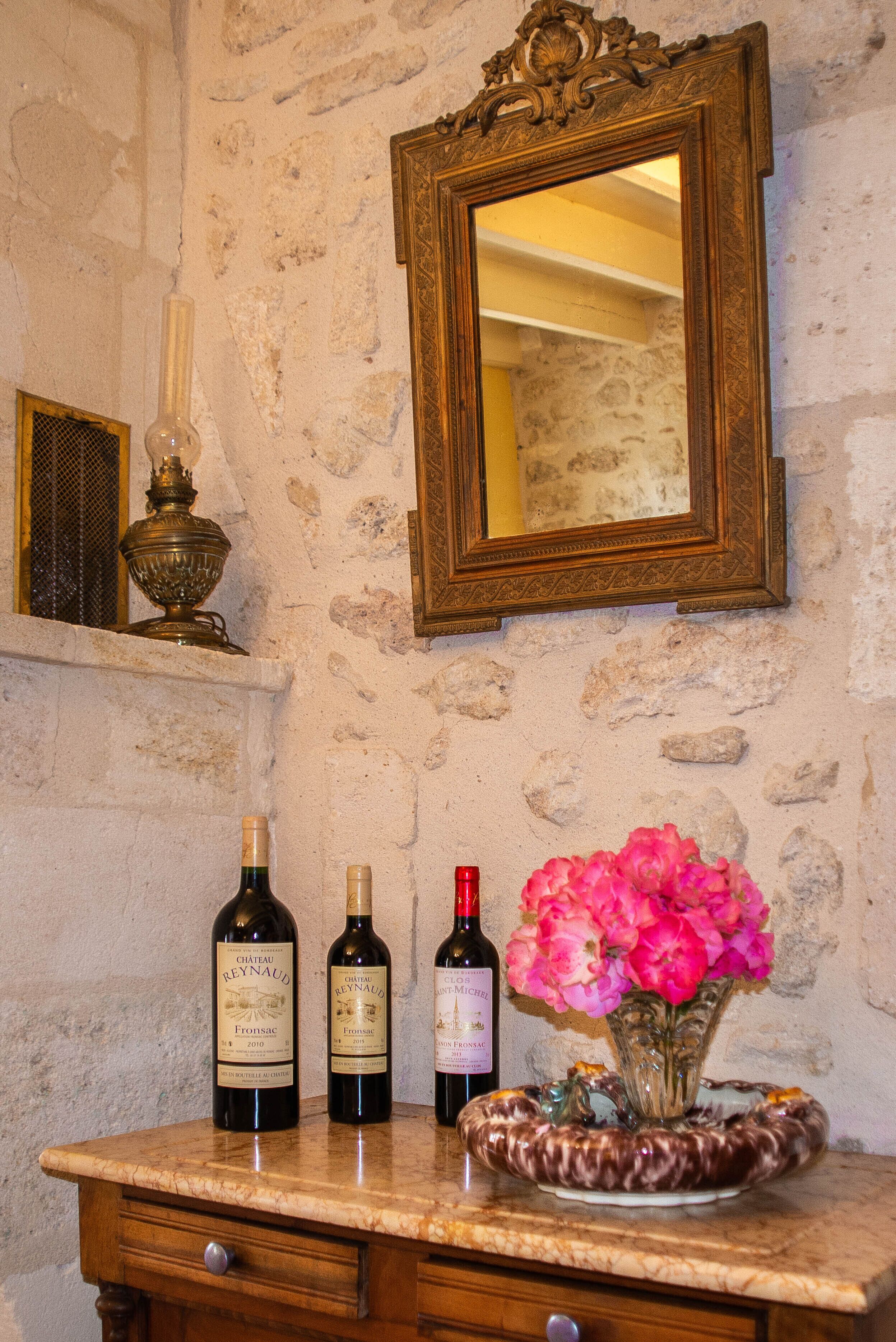 Una encimera de mármol con tres botellas de vino y un jarrón de flores rosadas.