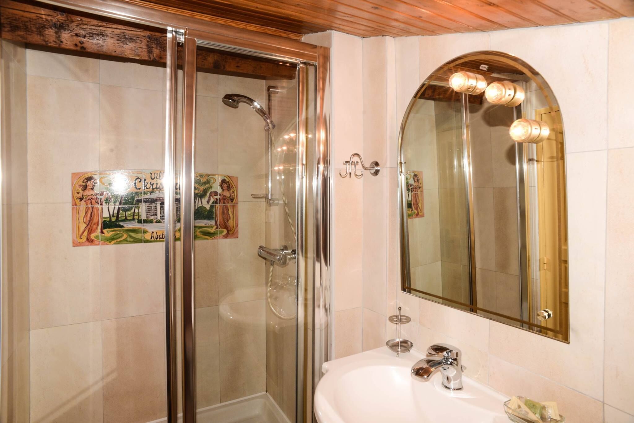 A bathroom with a glass-enclosed shower, a white sink, and a mirror with lights.