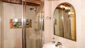 A bathroom with a glass-enclosed shower, a white sink, and a mirror with lights.