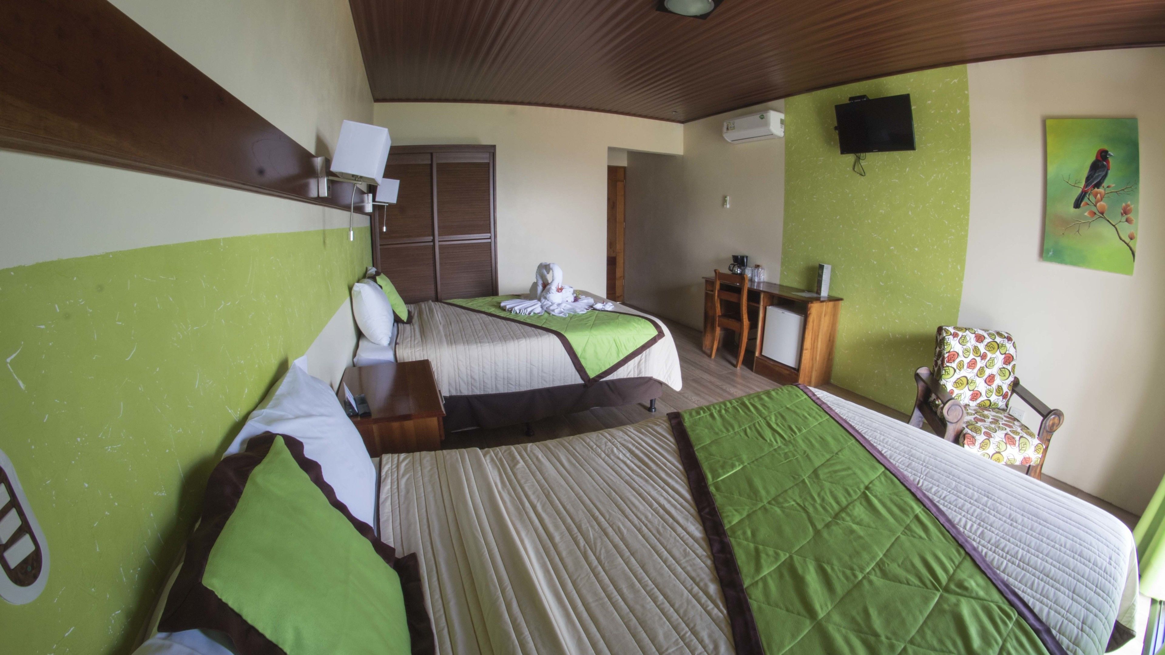 A hotel room with two beds, a desk, a chair, a television, and a wall-mounted air conditioner.