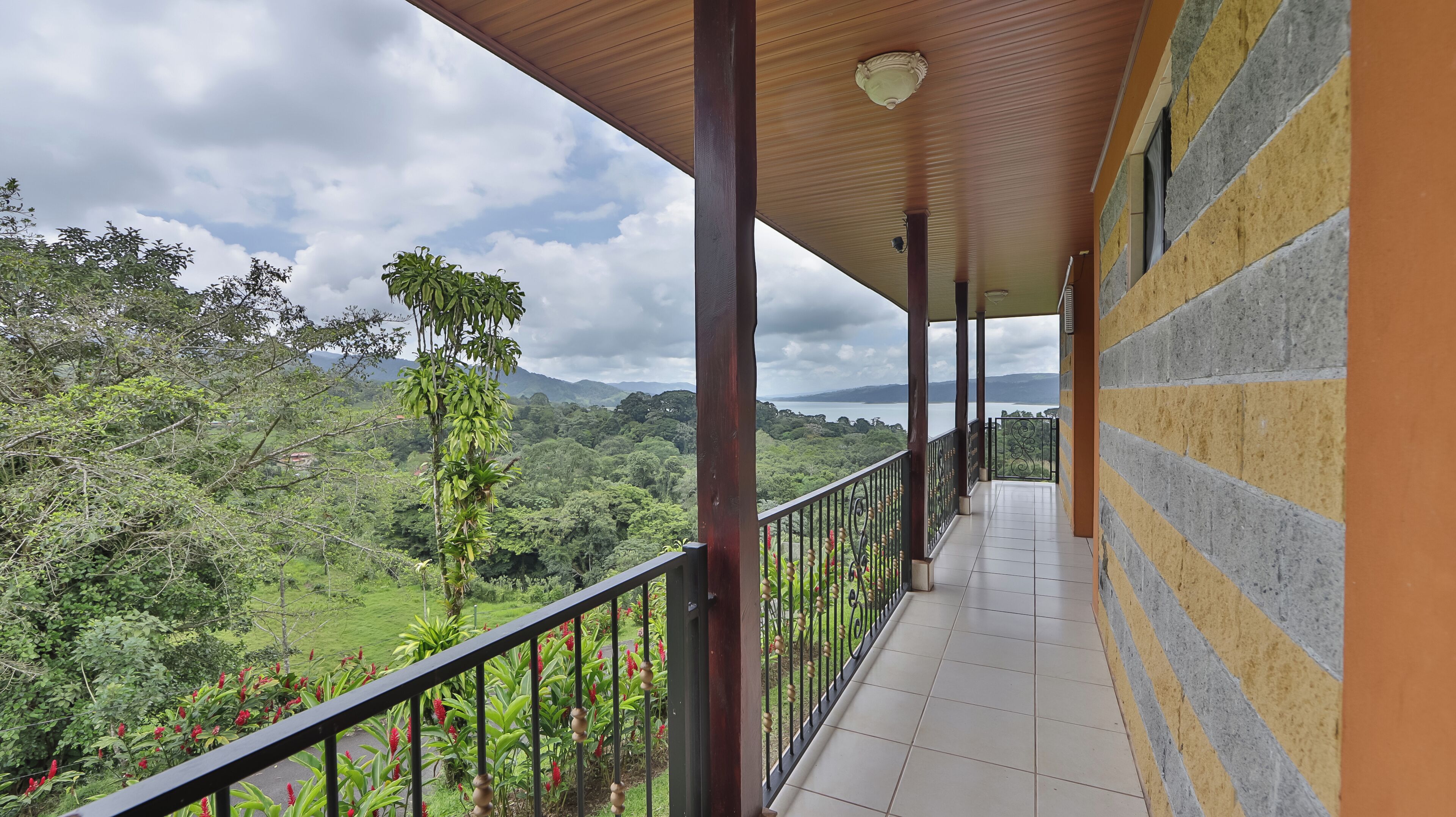 A covered balcony with a view of a lush green landscape and mountains.