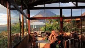 An outdoor dining area with tables and chairs, a greenhouse, and a mountain view. - Hotel Linda Vista (La Fortuna)