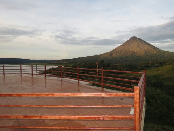 A terrace with a metal railing overlooking a landscape with a mountain.