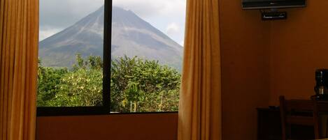 Habitación de hotel con techo de madera, un ventanal con cortinas, televisor de pantalla plana y cama con toallas y flores.