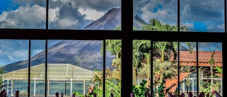 A restaurant with a view of mountains and a greenhouse. Tables are set with white tablecloths and purple napkins.