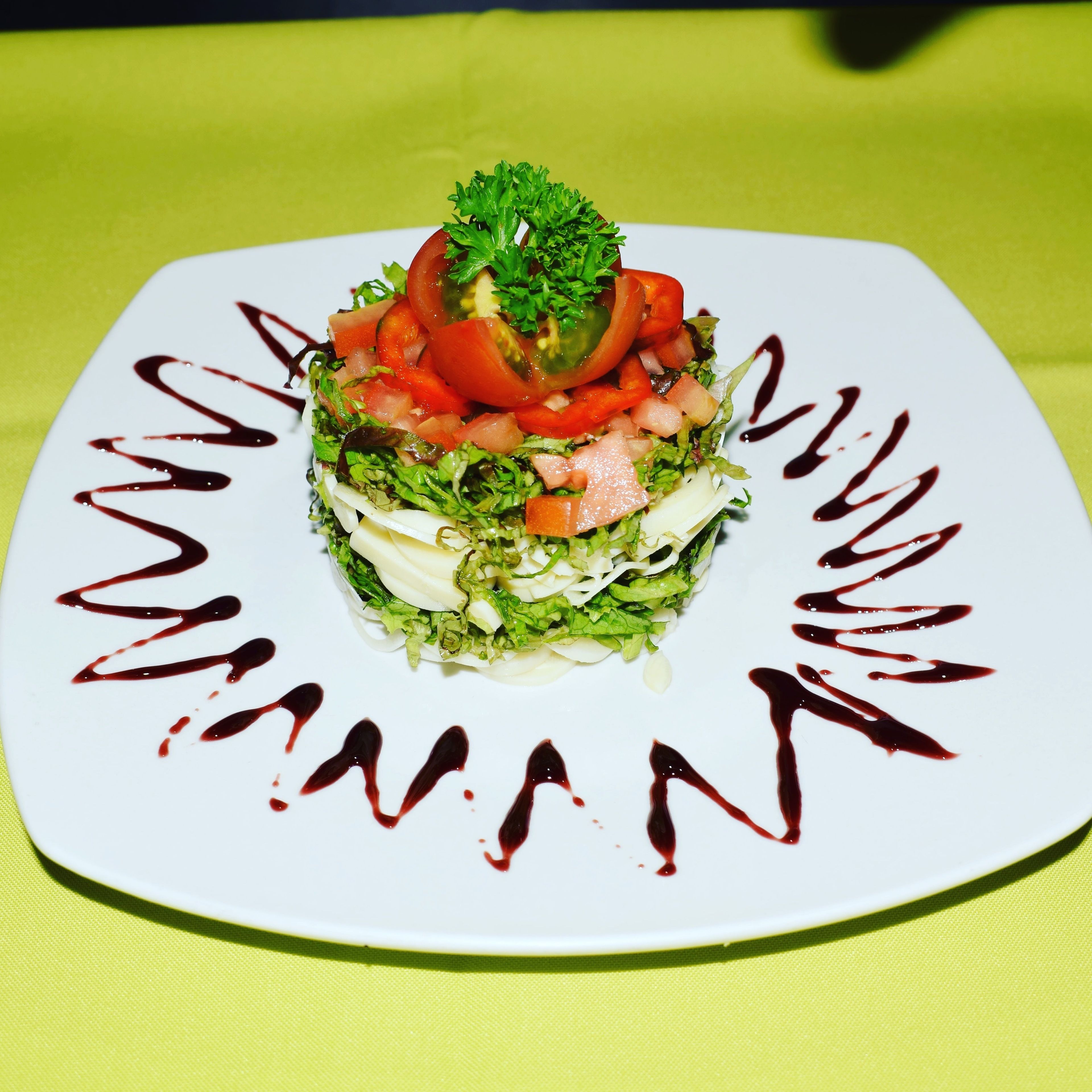 A square plate with a layered salad on a green tablecloth.
